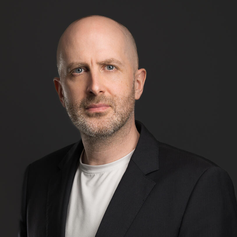 Head-shot of Simon Holmes, white male, mid-40's, no hair, salt and pepper stubble, blue eyes